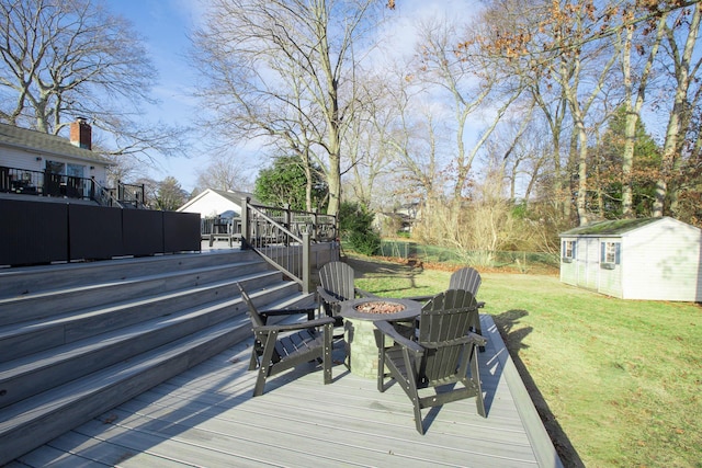 wooden deck featuring a lawn, an outdoor fire pit, and a shed