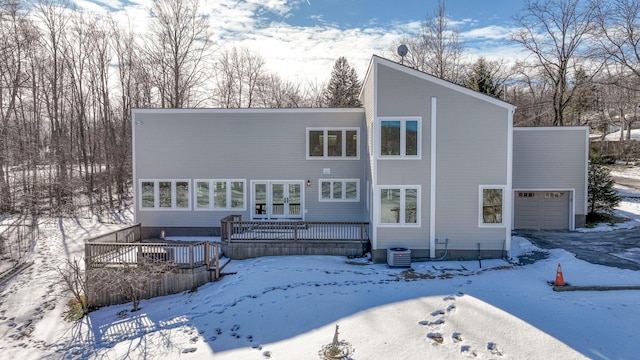 snow covered property with a garage, central AC, and a deck