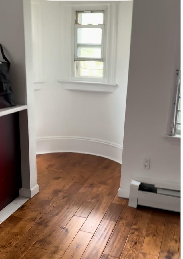 interior space with a baseboard heating unit and dark hardwood / wood-style flooring