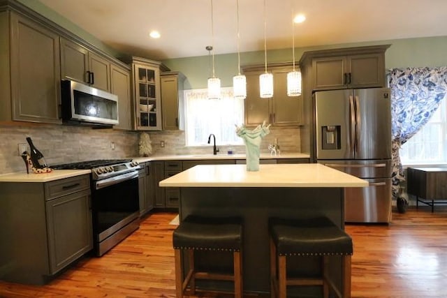 kitchen featuring light hardwood / wood-style floors, appliances with stainless steel finishes, a kitchen island, pendant lighting, and a breakfast bar