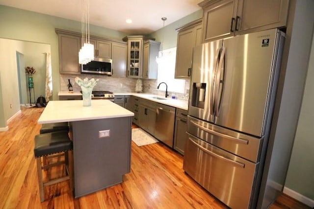 kitchen with gray cabinets, stainless steel appliances, a kitchen island, pendant lighting, and sink