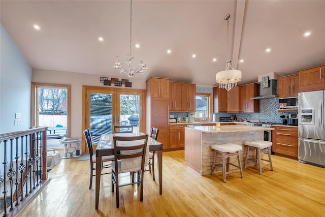 kitchen with appliances with stainless steel finishes, wall chimney range hood, pendant lighting, and a center island