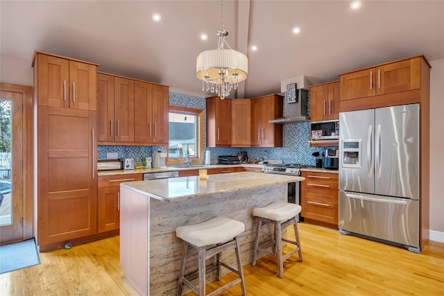 kitchen featuring appliances with stainless steel finishes, a center island, wall chimney exhaust hood, a kitchen bar, and decorative light fixtures