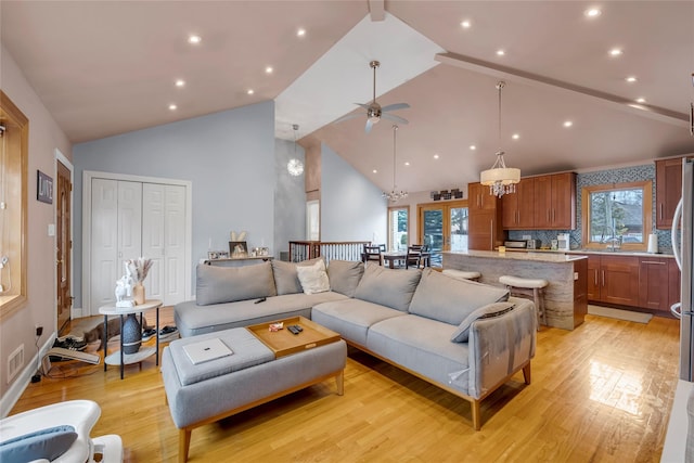 living room with ceiling fan, beamed ceiling, sink, light wood-type flooring, and high vaulted ceiling