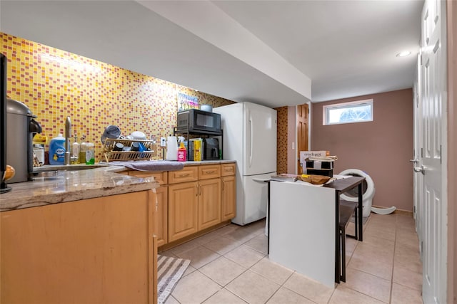 kitchen featuring backsplash, white fridge, light stone countertops, light tile patterned floors, and light brown cabinetry