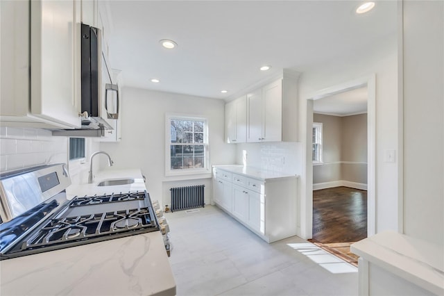 kitchen with light stone counters, radiator, gas stove, sink, and white cabinetry