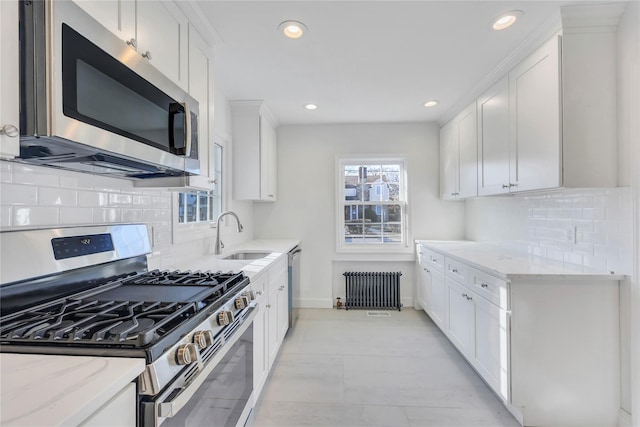 kitchen featuring white cabinetry, radiator heating unit, sink, stainless steel appliances, and light stone counters