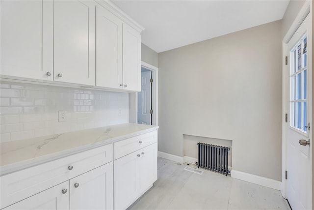 kitchen with white cabinets, decorative backsplash, light stone counters, and radiator