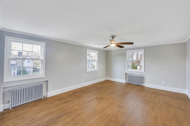 unfurnished living room featuring radiator heating unit, a wealth of natural light, crown molding, and wood-type flooring