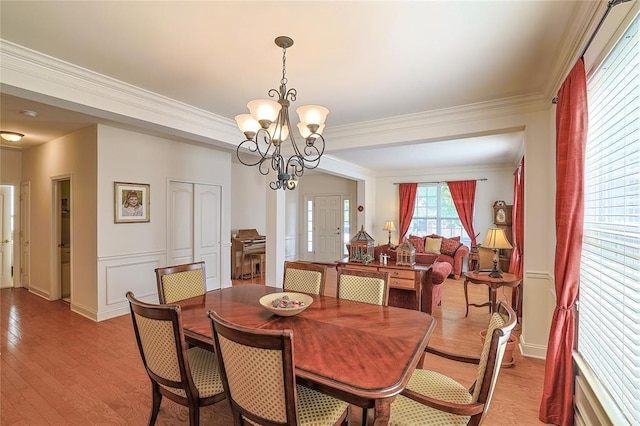 dining area with light wood-type flooring, an inviting chandelier, and crown molding