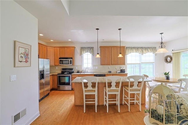 kitchen with stainless steel appliances, sink, decorative light fixtures, light hardwood / wood-style floors, and a kitchen island