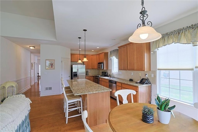 kitchen with decorative backsplash, appliances with stainless steel finishes, light stone countertops, pendant lighting, and a center island