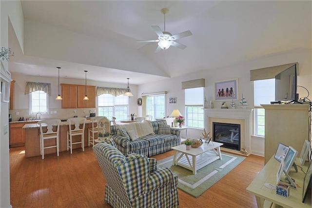 living room with ceiling fan, sink, light hardwood / wood-style floors, and lofted ceiling