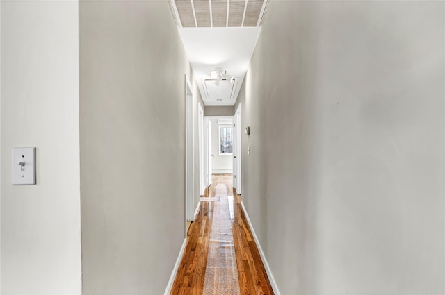 corridor featuring baseboards, wood finished floors, visible vents, and attic access