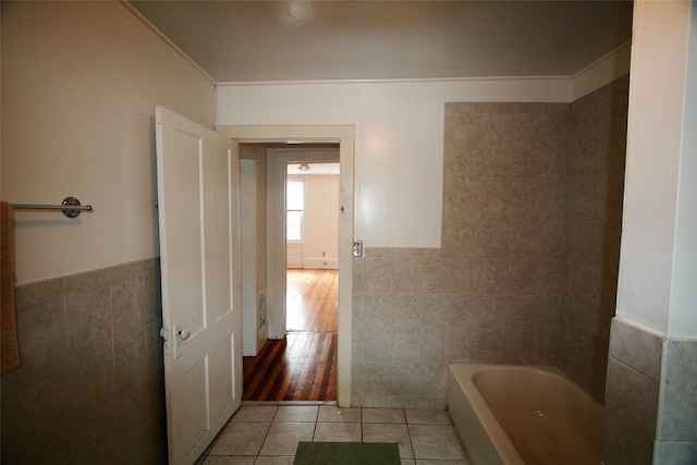 bathroom featuring a tub to relax in, tile patterned flooring, tile walls, and ornamental molding