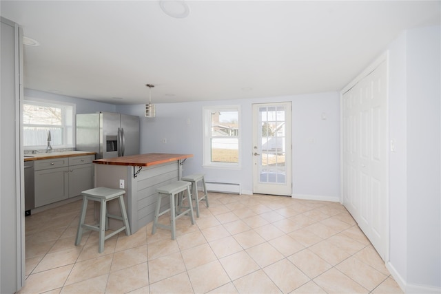 kitchen with pendant lighting, butcher block countertops, gray cabinets, a breakfast bar area, and stainless steel appliances