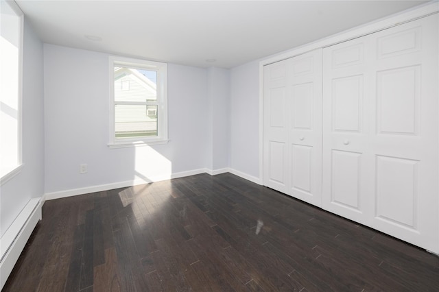 unfurnished bedroom with baseboard heating, dark hardwood / wood-style flooring, and a closet