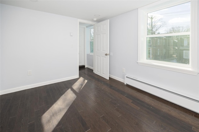 spare room featuring a baseboard heating unit and dark hardwood / wood-style flooring