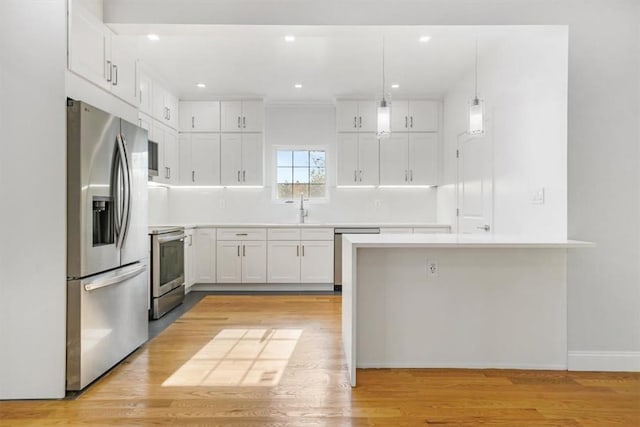 kitchen featuring light hardwood / wood-style floors, pendant lighting, sink, appliances with stainless steel finishes, and white cabinets