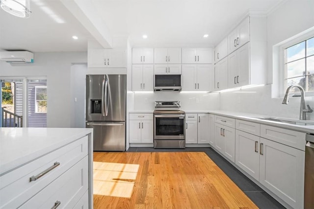 kitchen featuring appliances with stainless steel finishes, white cabinetry, sink, plenty of natural light, and a wall mounted air conditioner