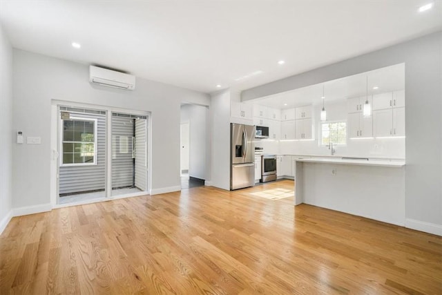 interior space with an AC wall unit, decorative light fixtures, white cabinetry, stainless steel appliances, and light wood-type flooring