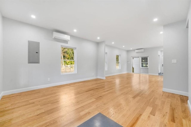 unfurnished living room with electric panel, light hardwood / wood-style floors, and a wall mounted air conditioner