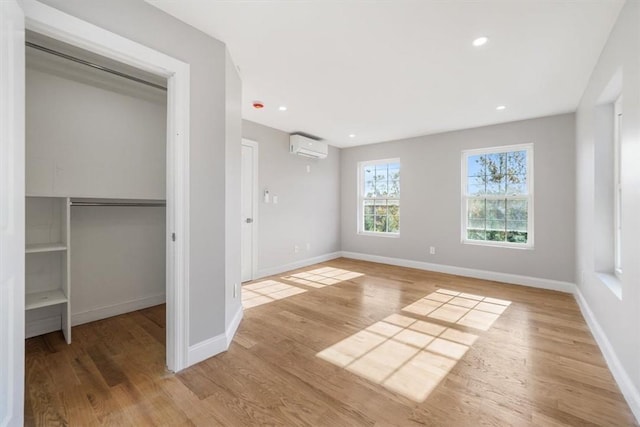 unfurnished bedroom with an AC wall unit, a closet, and light hardwood / wood-style flooring