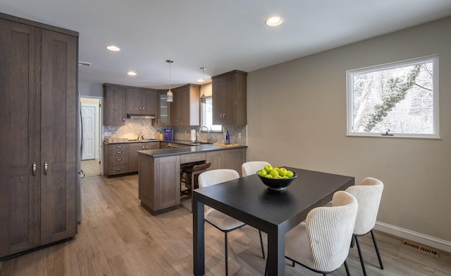 kitchen featuring sink, decorative backsplash, hanging light fixtures, kitchen peninsula, and light wood-type flooring