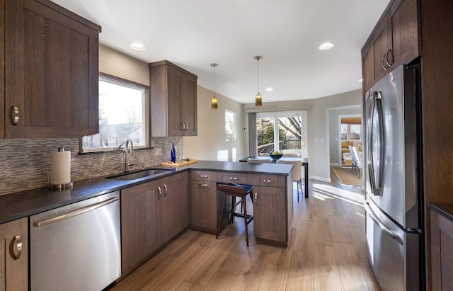 kitchen with sink, stainless steel appliances, light hardwood / wood-style floors, decorative light fixtures, and kitchen peninsula