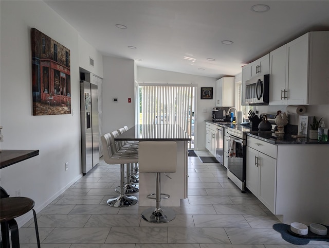 kitchen with stainless steel appliances, a kitchen island, vaulted ceiling, a kitchen bar, and white cabinets