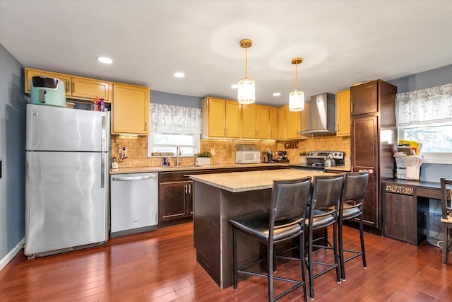 kitchen featuring appliances with stainless steel finishes, sink, wall chimney range hood, decorative light fixtures, and a center island