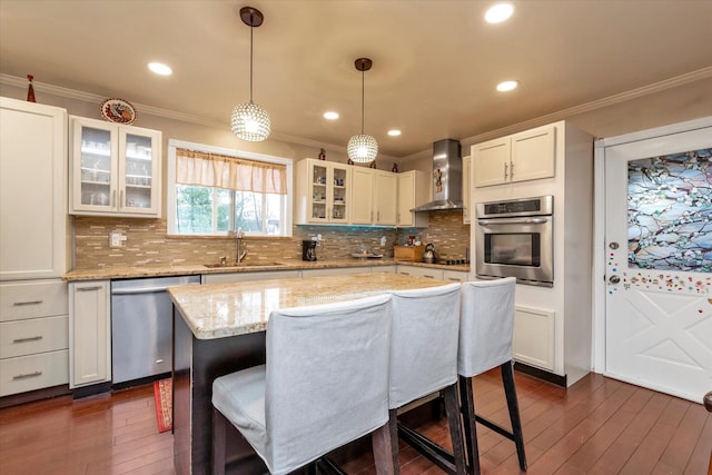 kitchen featuring white cabinetry, a center island, wall chimney exhaust hood, stainless steel appliances, and sink