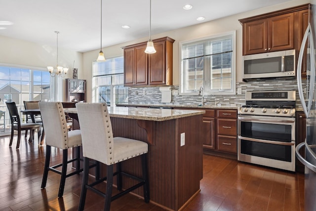 kitchen with a center island, hanging light fixtures, appliances with stainless steel finishes, a notable chandelier, and light stone countertops