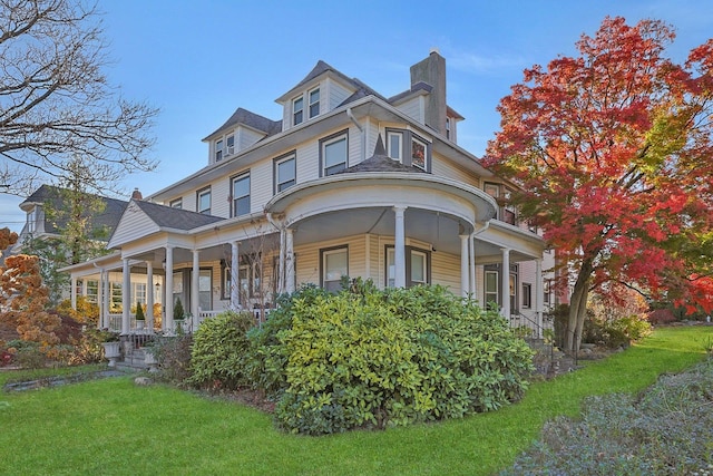 view of front facade with a front yard, covered porch, and a chimney