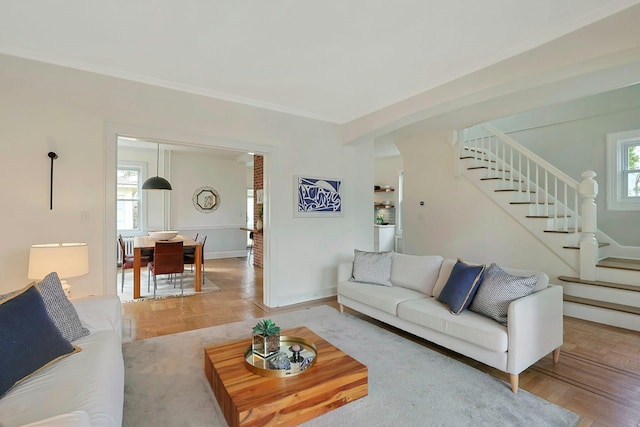 living room with plenty of natural light, crown molding, stairs, and baseboards