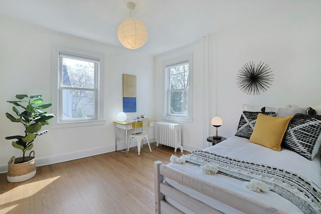 bedroom featuring baseboards, multiple windows, radiator, and hardwood / wood-style floors