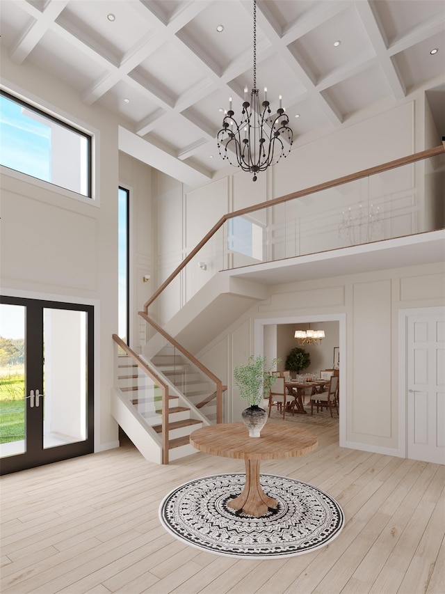 foyer entrance with a towering ceiling, stairway, an inviting chandelier, light wood-style floors, and a decorative wall