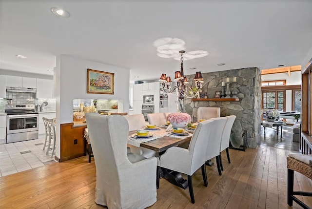 dining area with an inviting chandelier, a stone fireplace, and light hardwood / wood-style floors