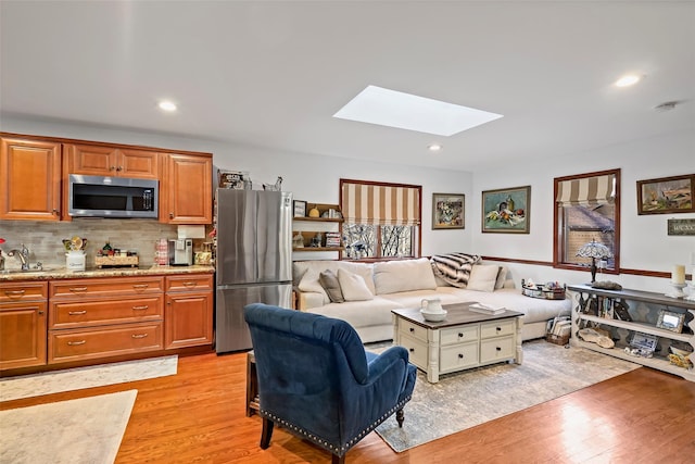 living room with a skylight, sink, and light wood-type flooring