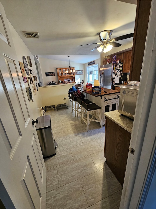 kitchen with pendant lighting, ceiling fan with notable chandelier, and stainless steel fridge