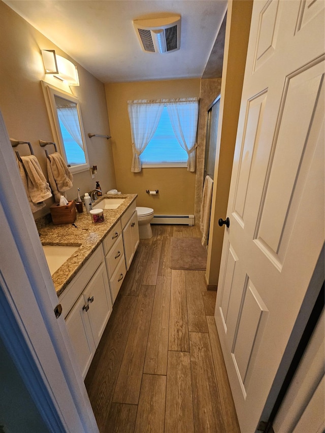 bathroom featuring baseboard heating, wood-type flooring, toilet, a shower with door, and vanity