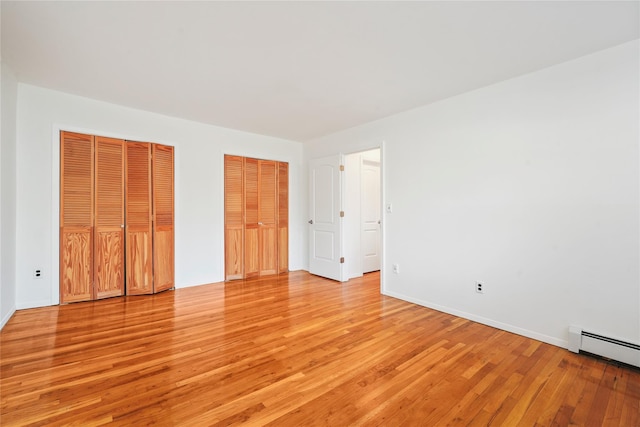 unfurnished bedroom featuring a baseboard heating unit, light hardwood / wood-style flooring, and multiple closets