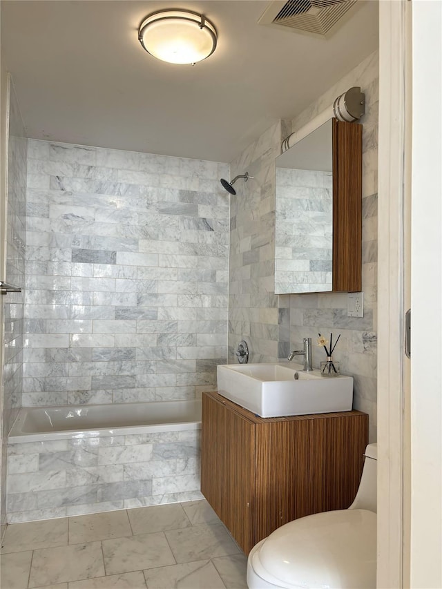 full bathroom featuring tile walls, vanity, tiled shower / bath combo, and toilet