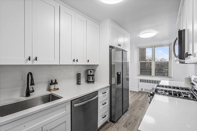 kitchen featuring radiator heating unit, sink, light hardwood / wood-style flooring, appliances with stainless steel finishes, and white cabinetry