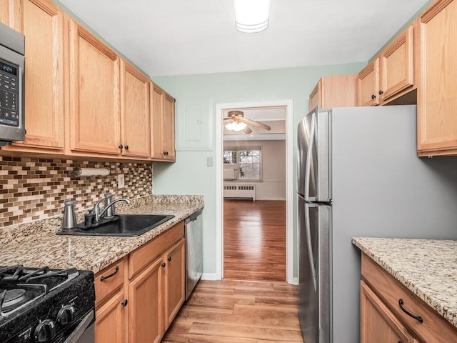 kitchen featuring radiator, stainless steel appliances, ceiling fan, and light stone counters