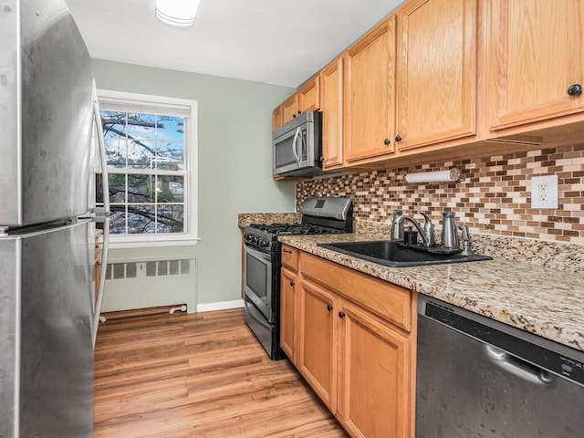 kitchen featuring stainless steel appliances, light hardwood / wood-style floors, backsplash, radiator heating unit, and sink