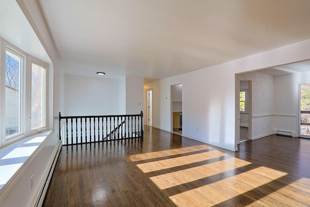 empty room featuring dark hardwood / wood-style floors, a wealth of natural light, and a baseboard heating unit