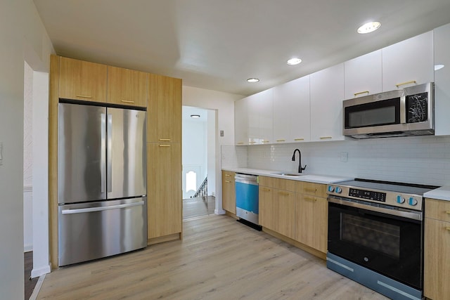 kitchen featuring appliances with stainless steel finishes, light wood-type flooring, backsplash, sink, and white cabinets