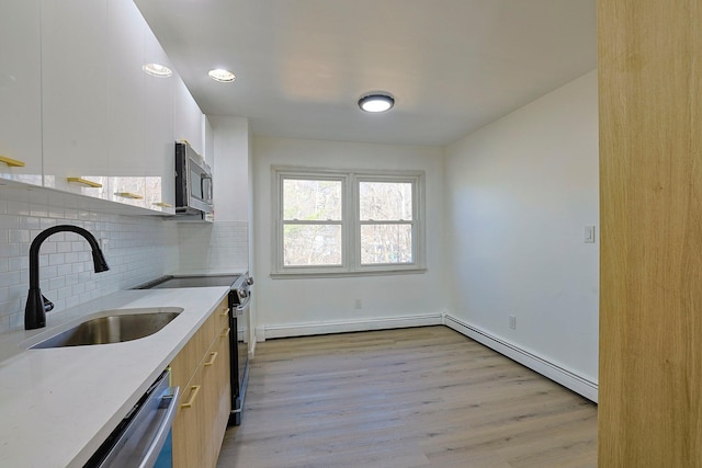 kitchen with sink, stainless steel appliances, a baseboard radiator, decorative backsplash, and light wood-type flooring