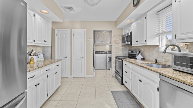 kitchen featuring washer and clothes dryer, white cabinets, sink, light stone counters, and stainless steel appliances